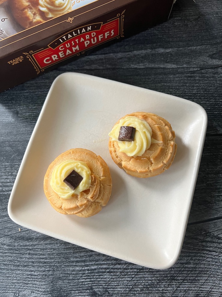 2 cream puffs on a white plate with the Italian Custard Cream Puff box in the background.