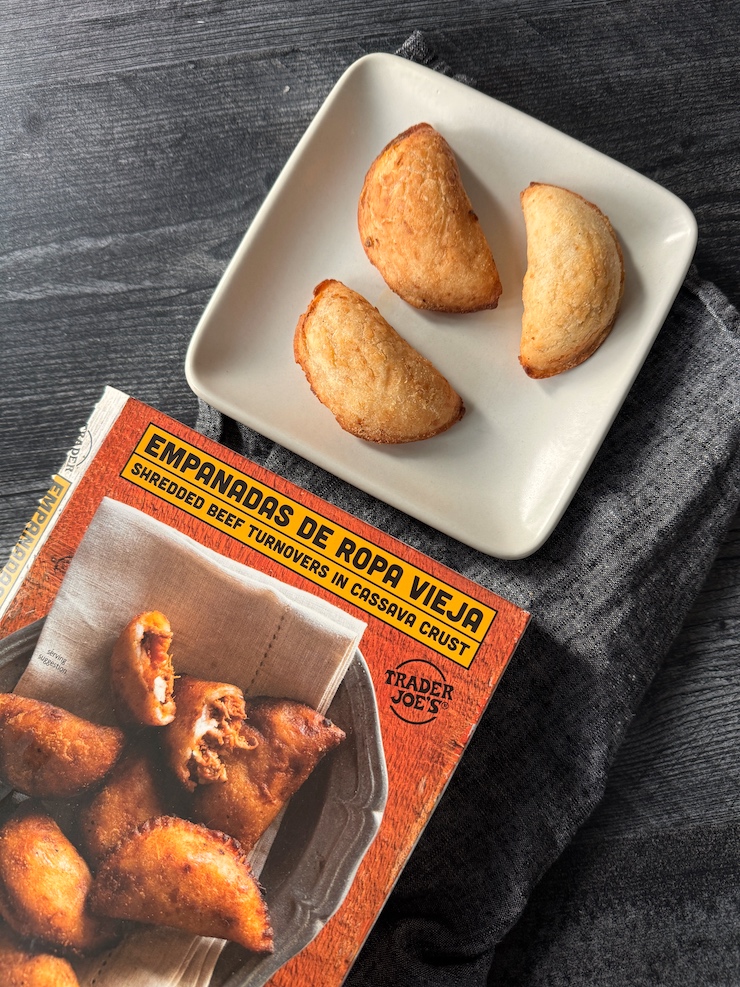 3 mini empanadas on a white plate next to a box labeled Empanadas de Ropa Vieja.