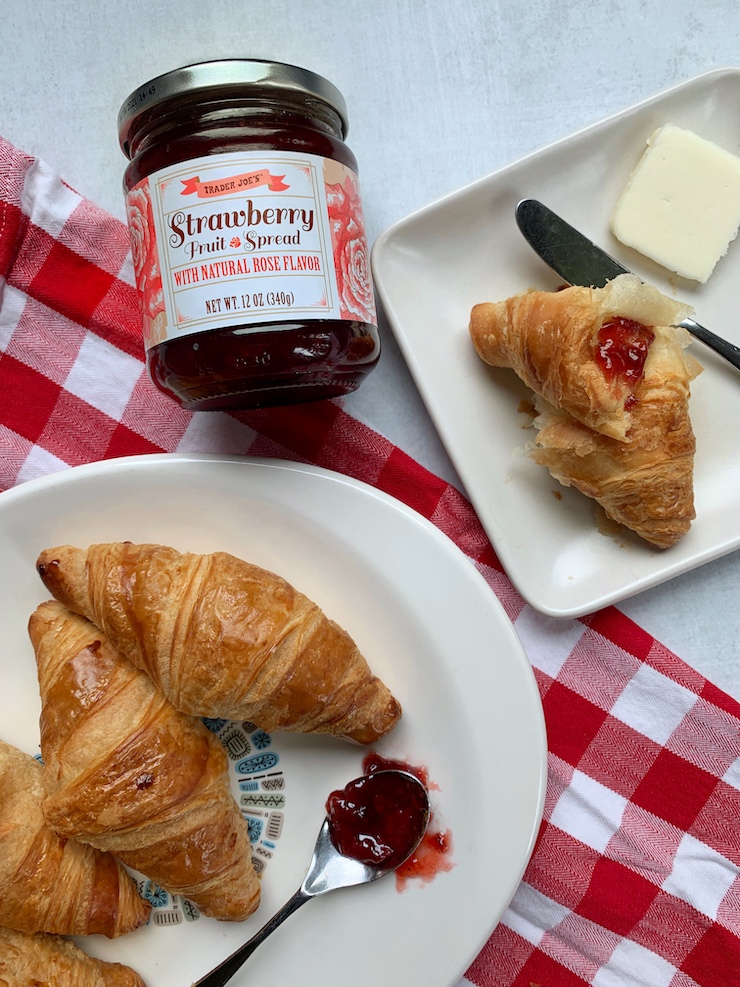 A jar of Trader Joe's strawberry rose fruit spread is arranged next to a platter of 4 croissants.