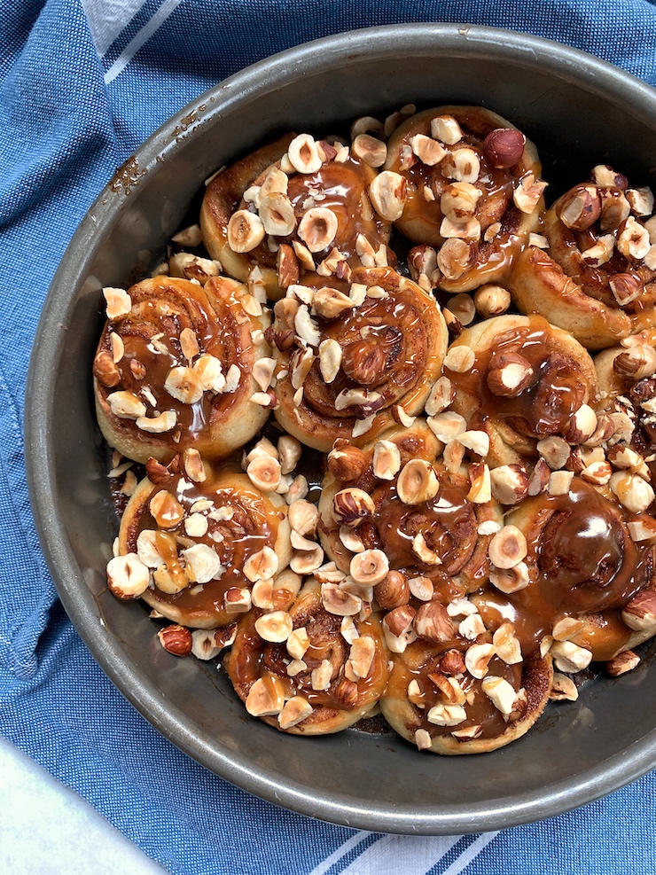 Three-quarter view of a pan of sticky buns with Trader Joe's Cinnamon Bun Spread and hazelnuts.