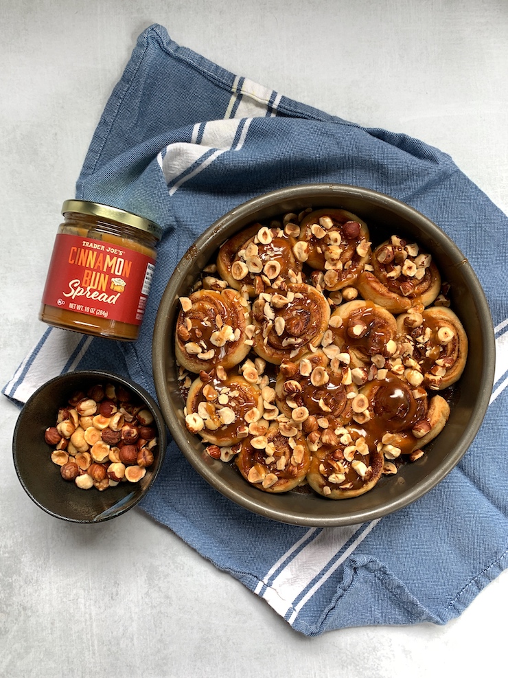 Trader Joe's Cinnamon Spread jar with a pan of sticky buns topped with hazelnuts.