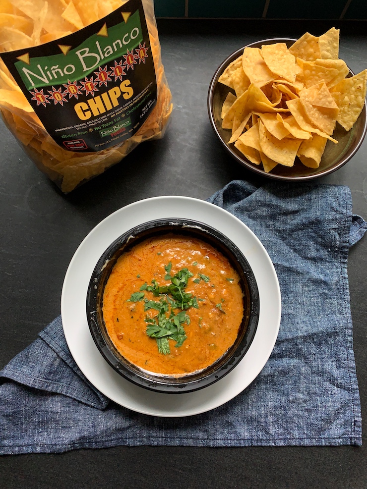 trader joe's queso fundido in a black bowl with tortiilla chips on the side