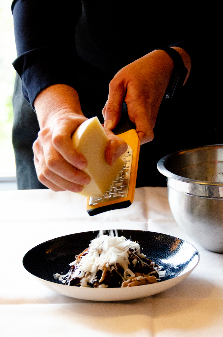 chef grates pecorino toscano over a radicchio salad.