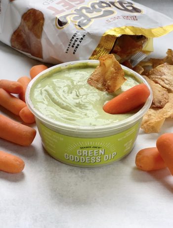 Trader Joe's Green Goddess dip in a tub with a potato chip and carrot stick in it.