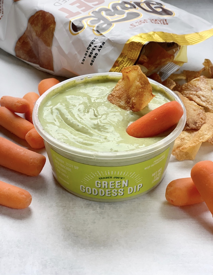 A tub of Trader Joe's Green Goddess dip pictured with a potato chip and a carrot stick in it. 