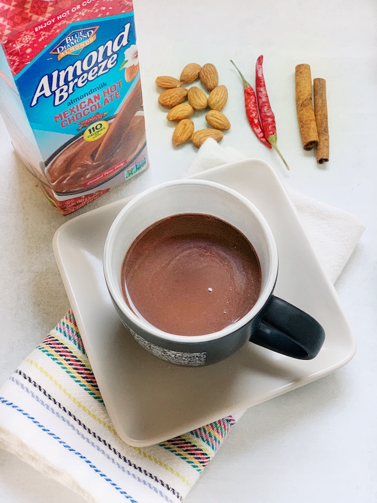 Almond Breeze Mexican Hot Chocolate in a mug next to a carton of the product.