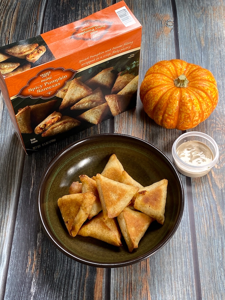 Mini spicy pumpkin samosas piled in a brown bowl with the packaging box set off to the left behind the bowl.