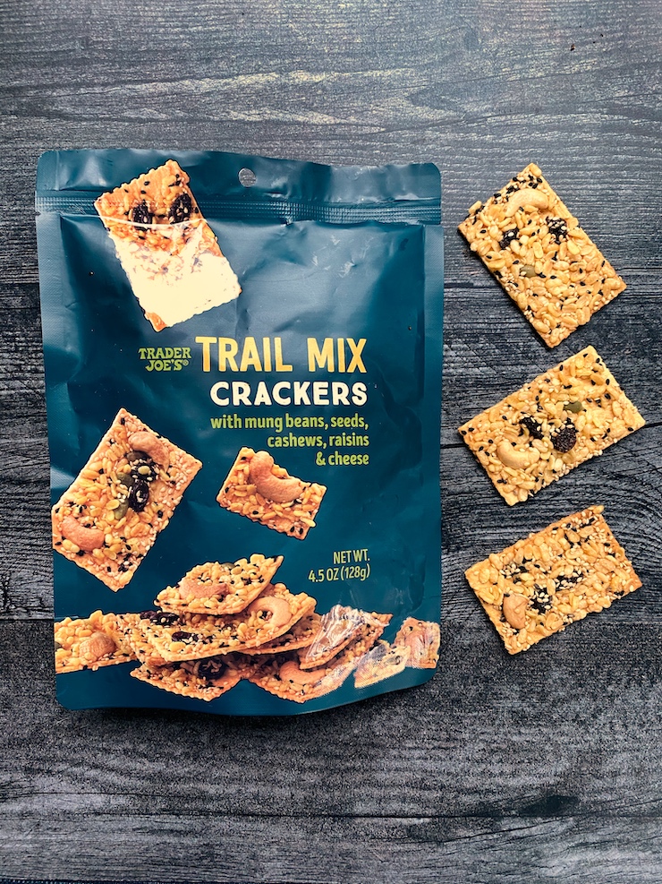 Dark blue-green bag of Trader Joe's Trail Mix crackers with three crackers arranged along the right side of the bag. 