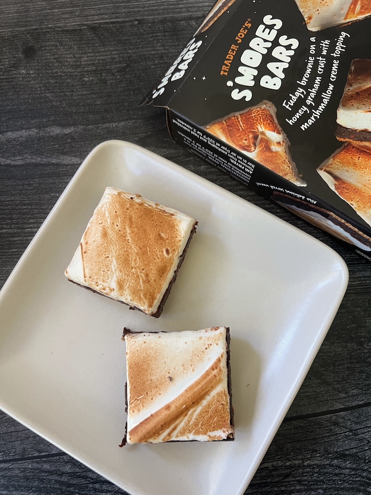 Two smores squares on a white plate shown with the box above them. 