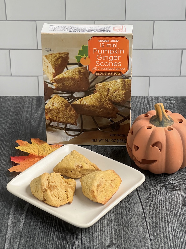 Box of Trader Joe's Mini Pumpkin Ginger Scones on a white plate  arranged with a smiling ceramic jack o'lantern, yellow and orange maple leaves