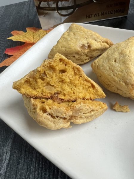 Mini Pumpkin Ginger Scone broken in half to show the interior on a white plate with two other scones. 