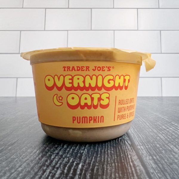 Trader Joe's Pumpkin Overnight Oats container on a white subway tile and weathered wood background. 