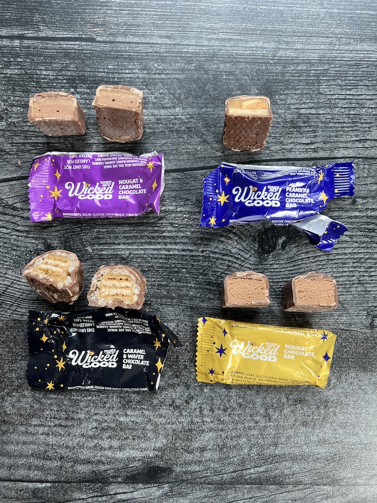 Cross sections of each Wicked Good bar shown with the wrappers on a weathered wood background. 