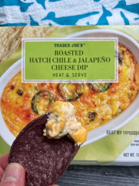 Blue corn chip dipped in the Hatch chile Jalapeno Cheese dip with the Package in the background. 