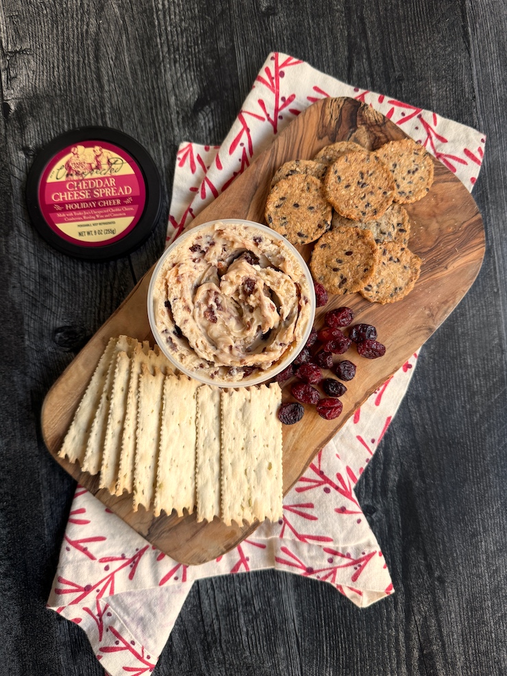Trader Joe's Holiday Cheer Cheddar Cheese spread open on a wood serving board surrounded by crackers and dried cranberries. 