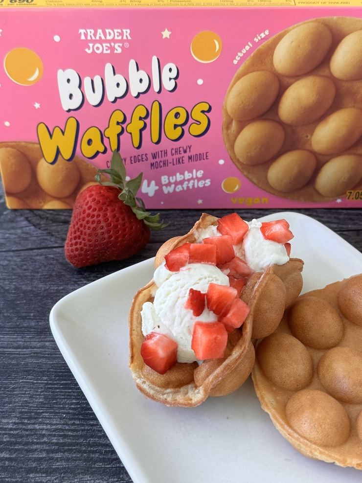 Trader Joe's Bubble Waffles box with one waffle bent into a taco shape with 2 small scoops of vanilla ice cream and diced strawberries.