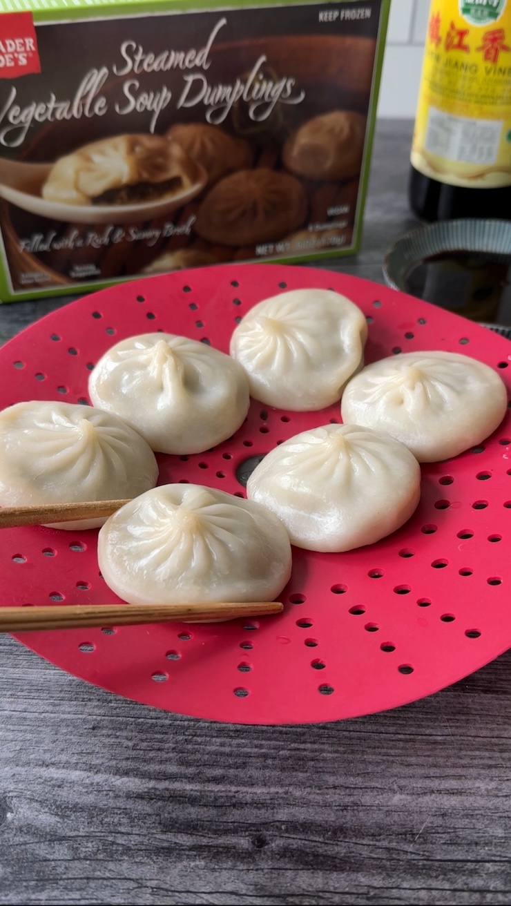 6 Trader Joe's Steamed Vegetable Soup Dumplings on a red silicon steamer basket with the box in the background.