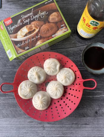 Overhead shot of Trader Joe's Steamed Vegetable Soup Dumplings (aka vegan XLB). The box is in the upper left corner, the dumplings are sitting on a red silicone steamer insert.