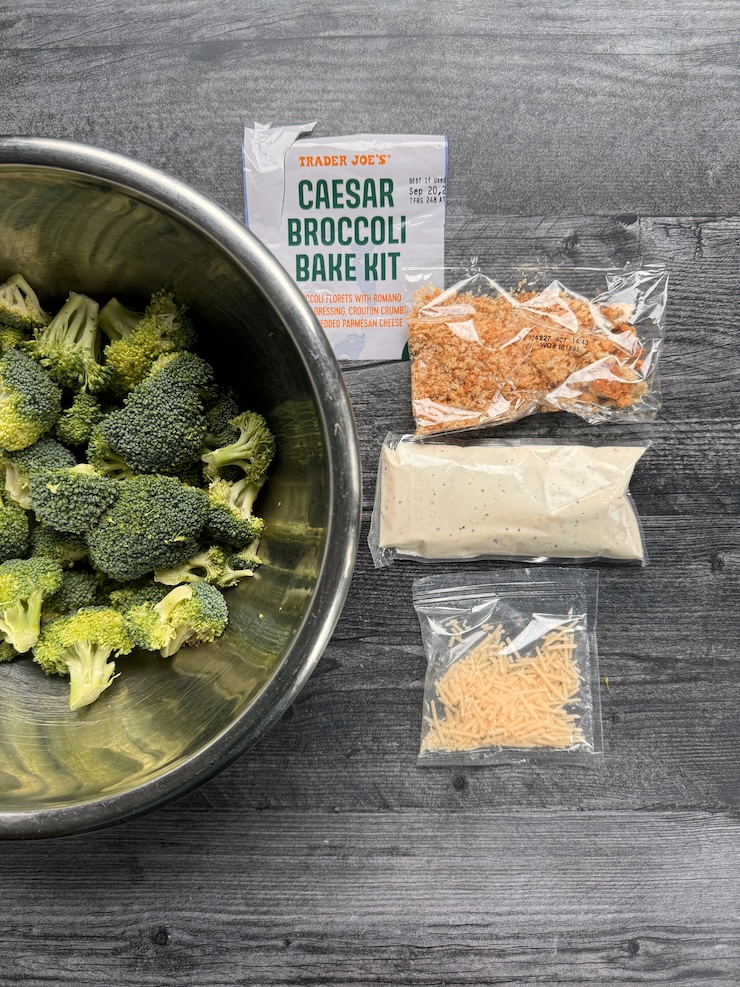 Trader Joe's Caesar Broccoli Bake Kit contents: broccoli in a stainless steel bol, packet of breadcrumb croutons, Caesar dressing, shredded parmesan cheese. ©DailyWaffle,LLC.