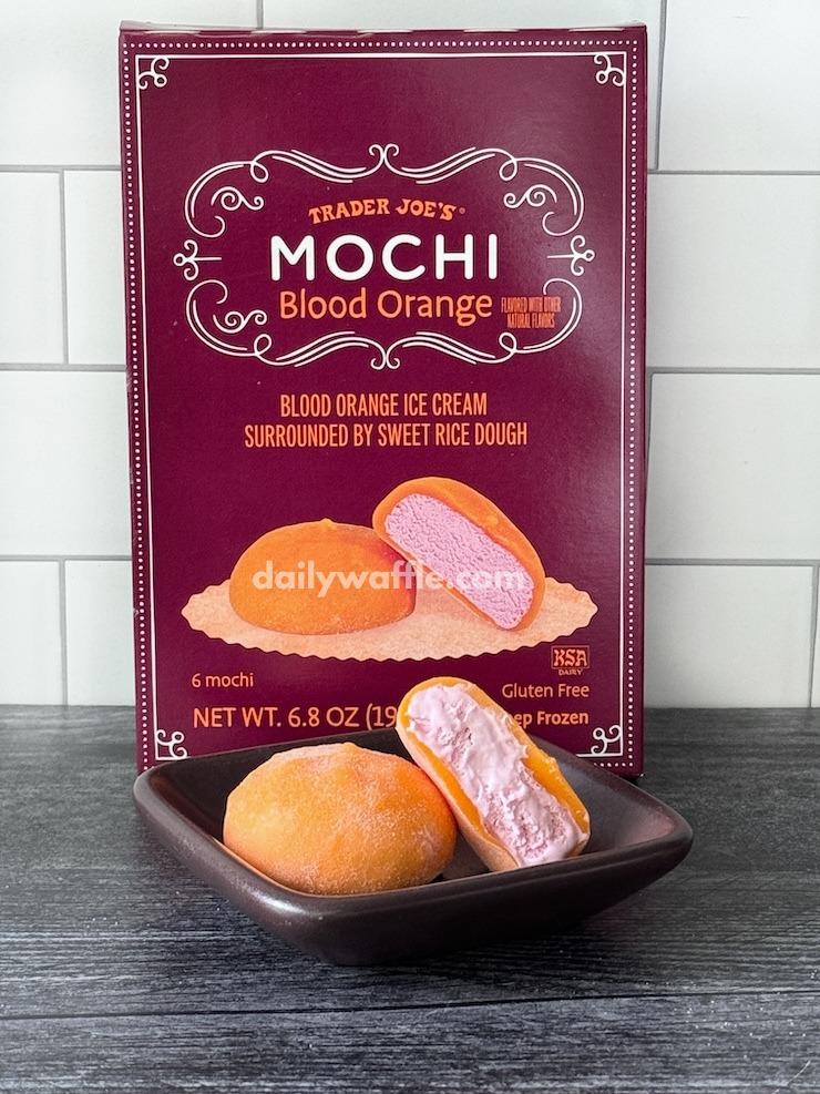 Trader Joe's Blood Orange Mochi Ice Cream box with a mochi and a cross section of one sitting on a small square brown plate.