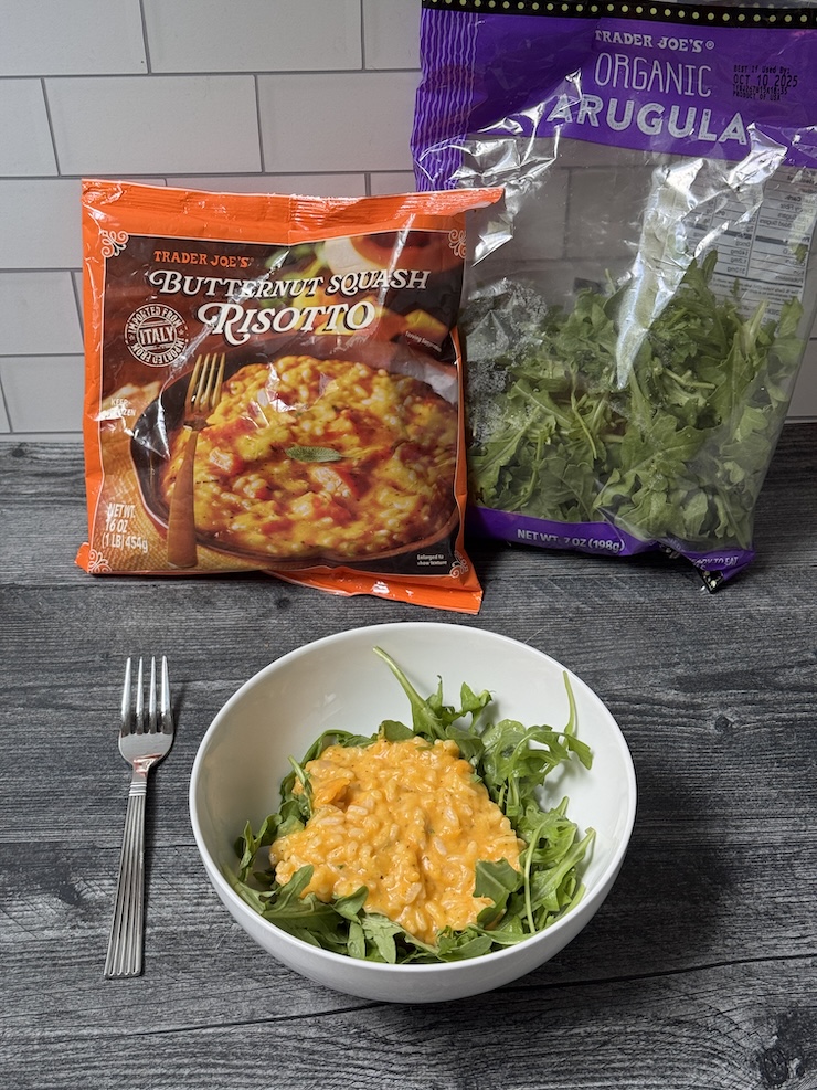 Trader Joe's Butternut Squash Risotto over arugula in a white bowl. Arugula bag and Butternut Squash Risotto bag in the background