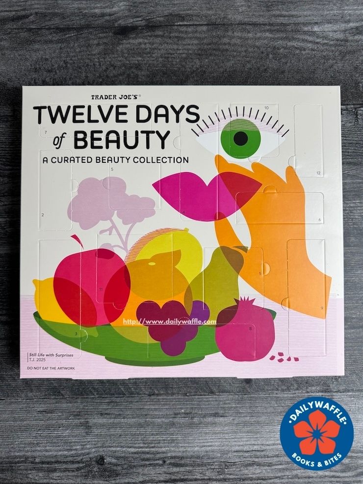 Trader Joe's 12 Days of Beauty. White rectangle box with an abstract design with a fruit bowl including apples, pear, pomegranate, lemon with a pair of lips and a green eye above it.