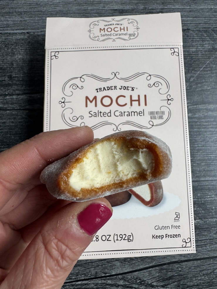 Trader Joe's Salted Caramel Mochi Ice Cream with a bite out of it,held over the top of the box.